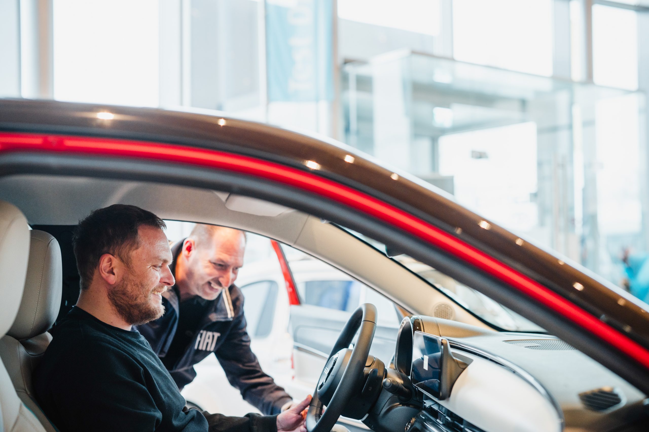 Kunde sitzt im Fahrzeug, während ein Mitarbeiter die Funktionen im Innenraum erklärt