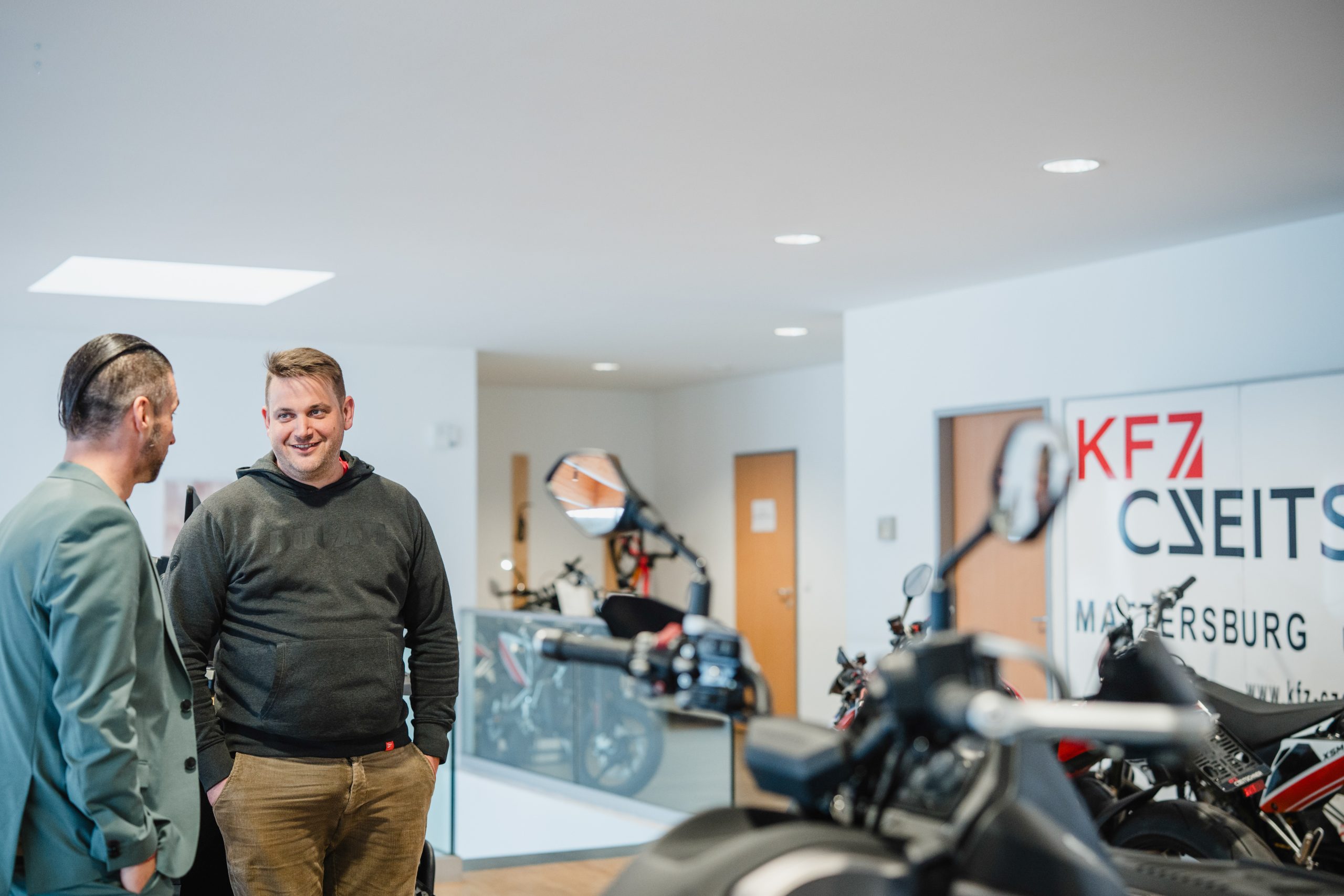 Zwei Personen sprechen im Schauraum von KFZ Czveitschner zwischen ausgestellten Motorrädern