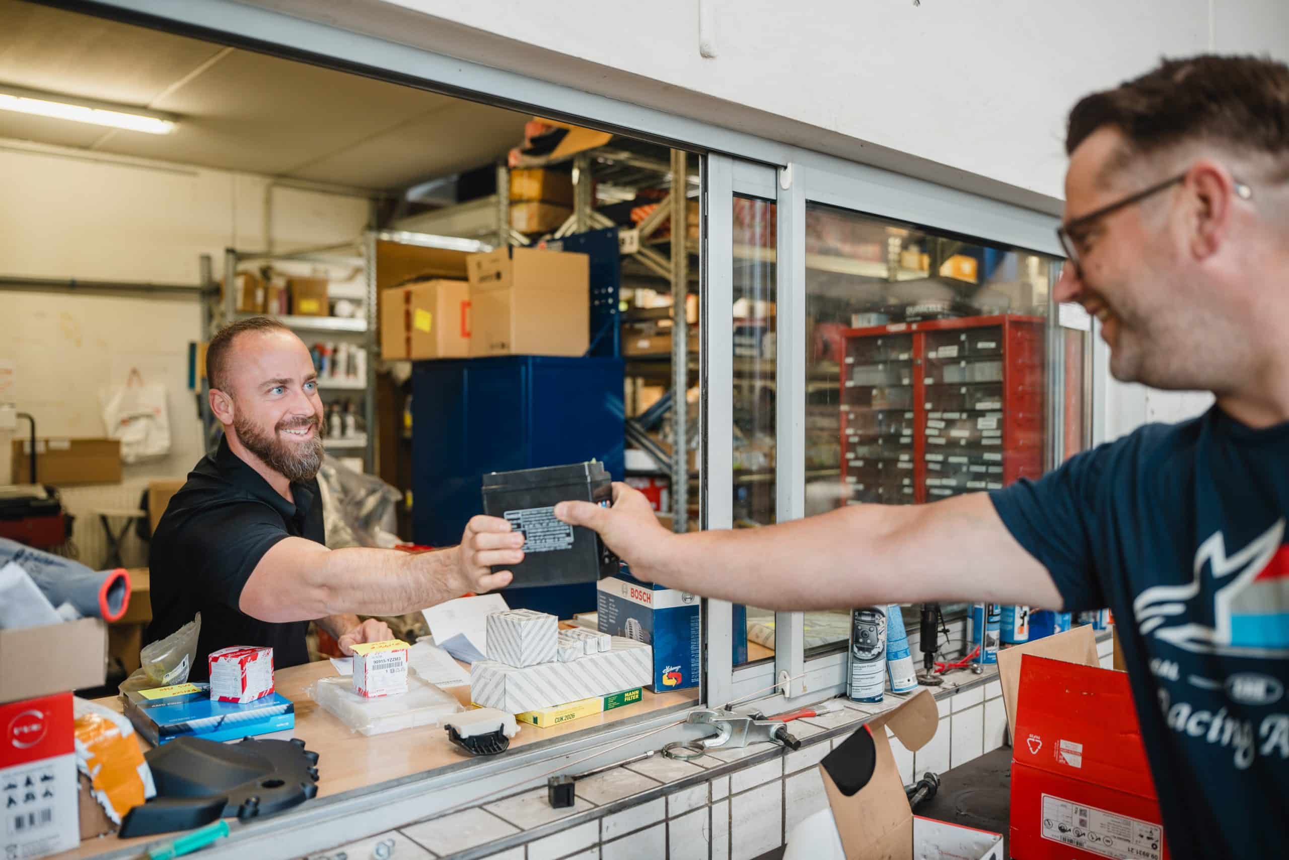 Mitarbeiter übergibt eine Autobatterie am Ersatzteillager einer KFZ-Werkstatt