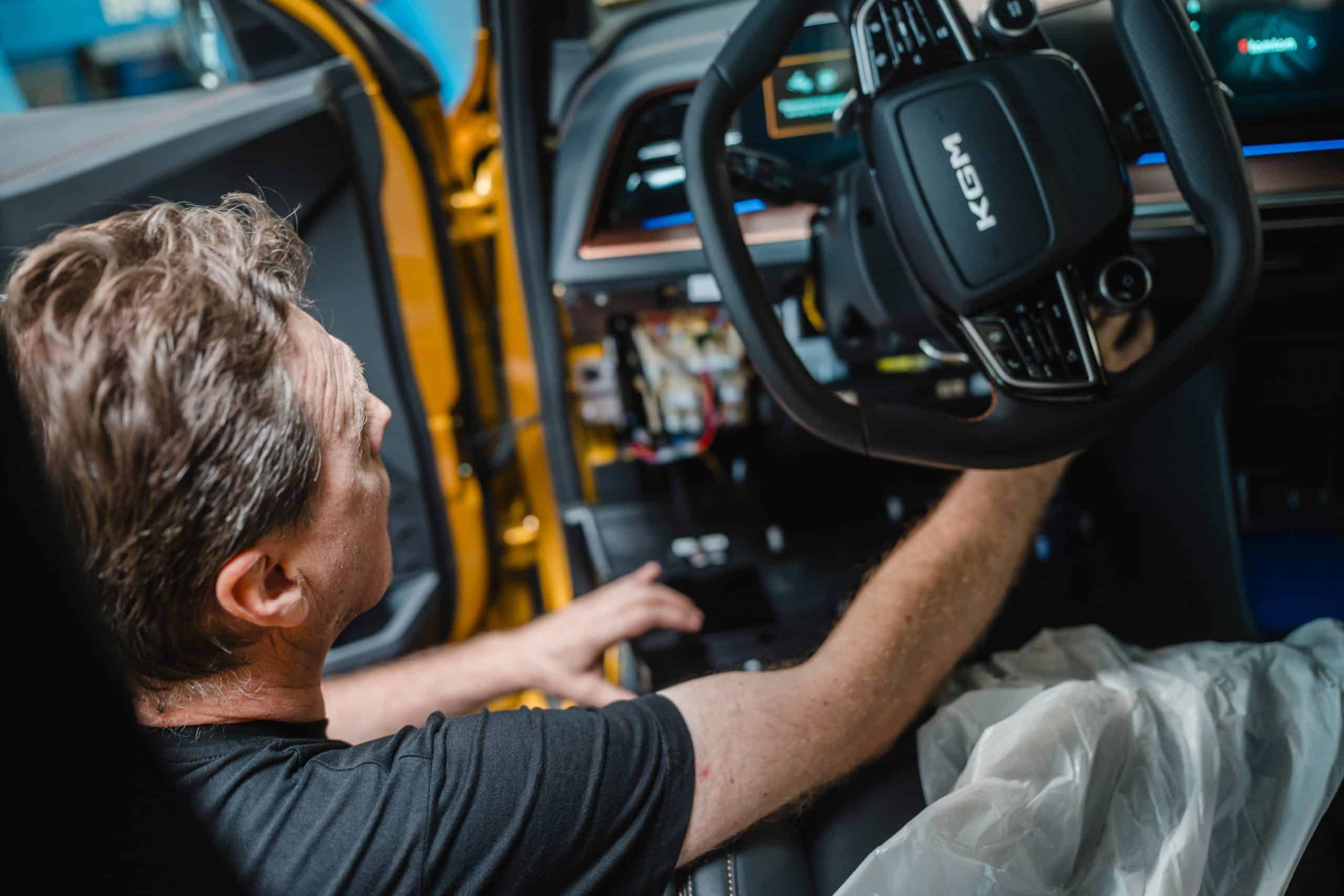Mitarbeiter arbeitet im Innenraum eines Fahrzeugs an der Elektronik und Diagnose