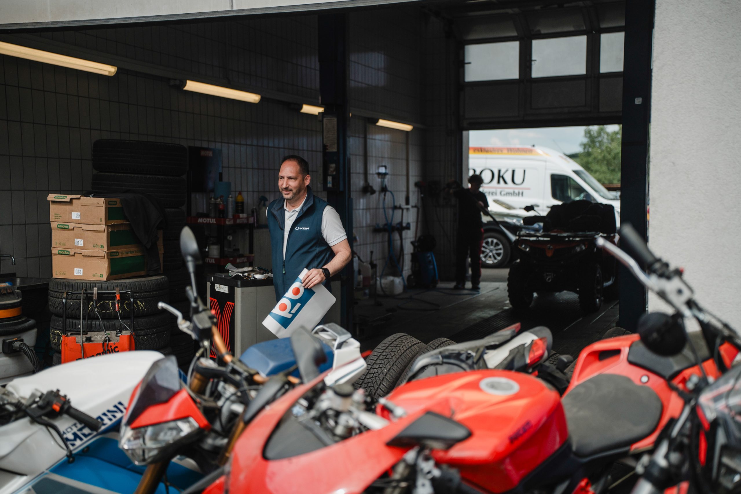 Mitarbeiter steht in einer Werkstatt zwischen Motorrädern und Reifen