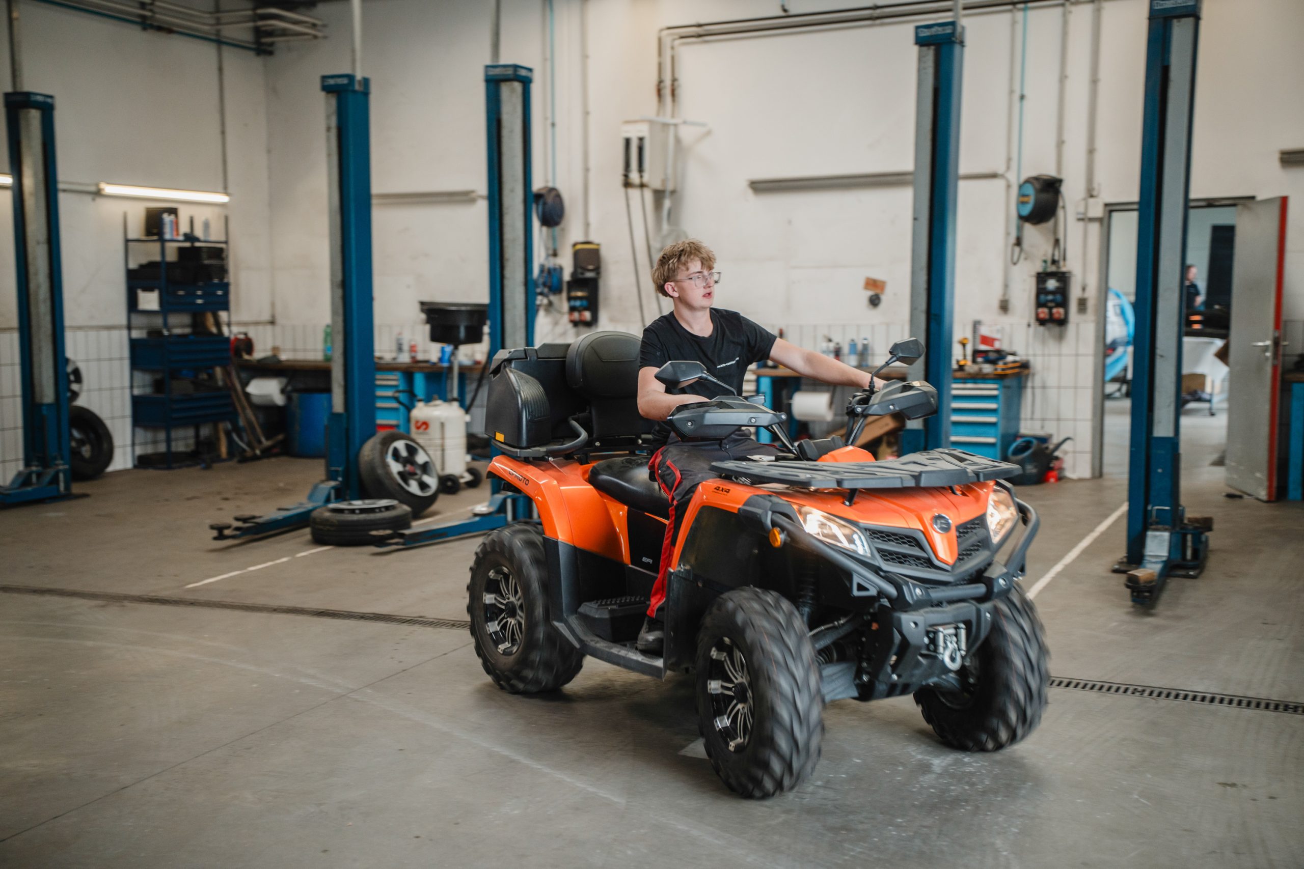 Mitarbeiter fährt ein orangefarbenes Quad durch eine KFZ-Werkstatt