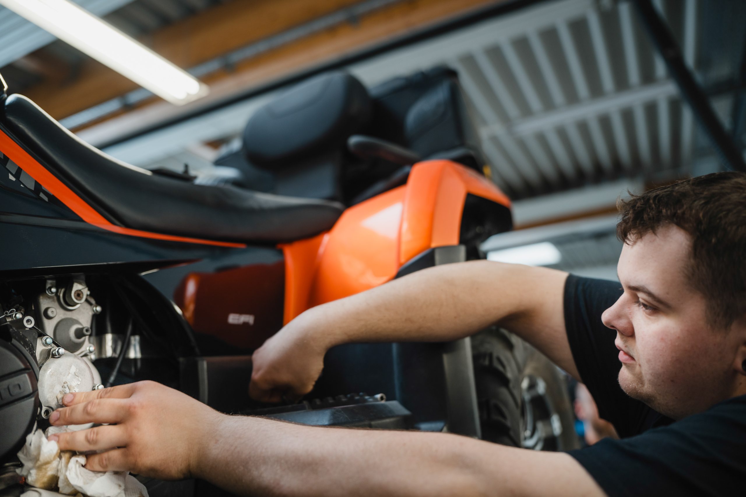 Mitarbeiter arbeitet an einem orangefarbenen Quad in einer KFZ-Werkstatt
