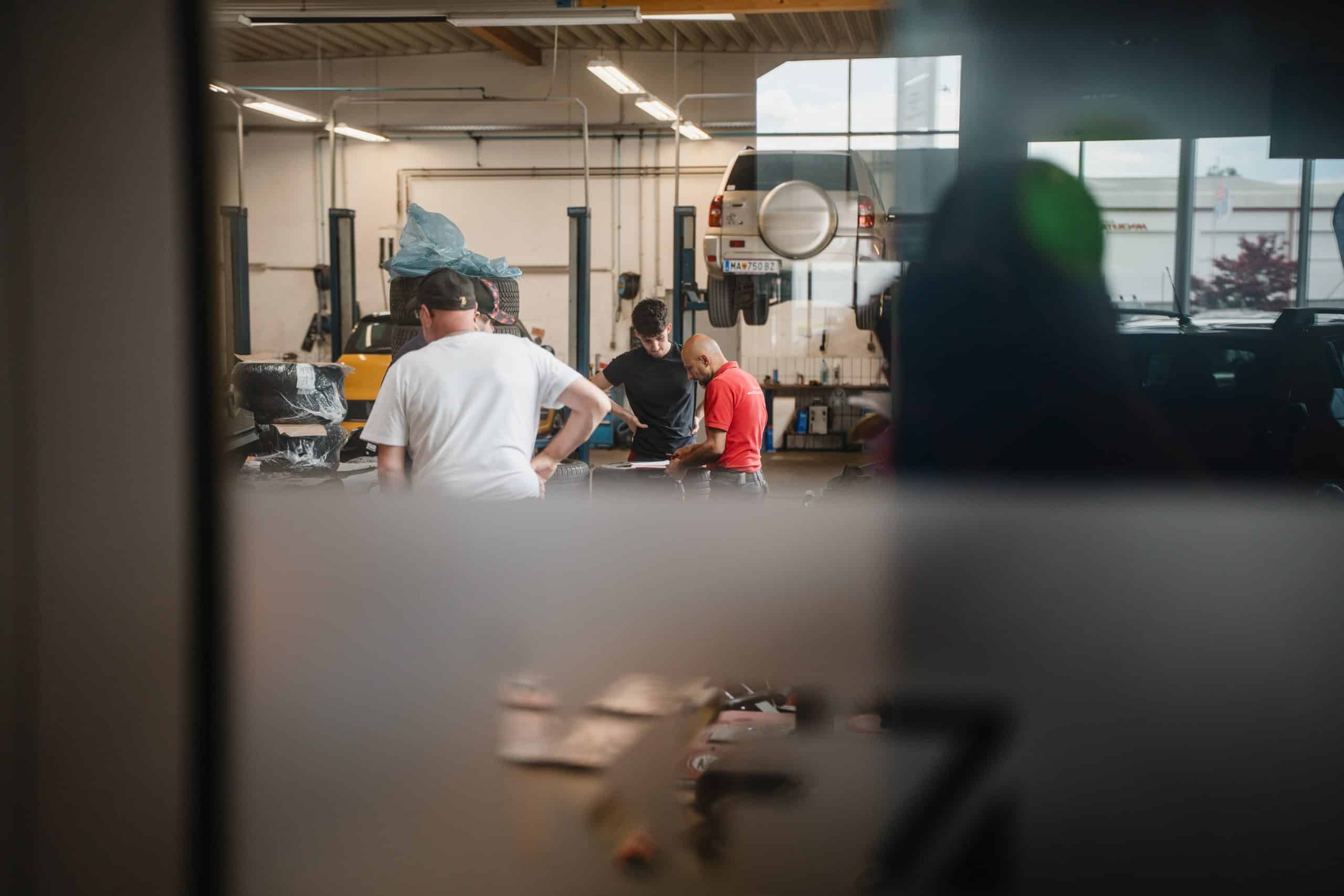 Mehrere Mitarbeiter besprechen Arbeiten an einem Fahrzeug in einer KFZ-Werkstatt